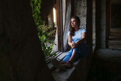 Young woman using phone while sitting on tree trunk