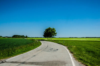 Road amidst field against clear blue sky