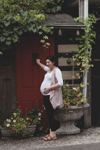 Side view of pregnant woman standing on footpath against houses