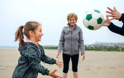 Woman with mother and daughter playing ball at beach against sky