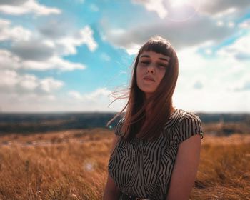 Beautiful young woman standing on field against sky