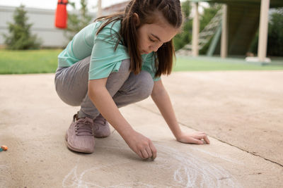Girl draws with colorful crayons on pavement. children's drawings with chalk on wall. creative kid. 