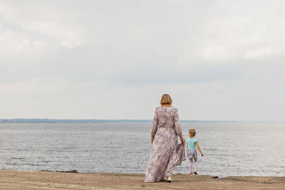 Rear view of woman standing at beach against sky