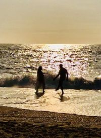 Silhouette women on beach against sky during sunset