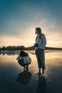 Couple standing on beach against sky during sunset
