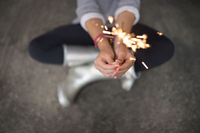 High angle view of girl holding sparkler while sitting on footpath