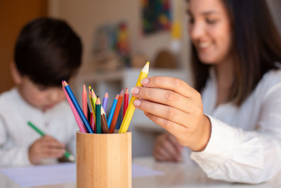 Smiling mother holding colored pencil sitting with son at home