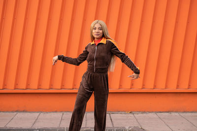 Cheerful african american woman in sportswear dancing in the street on an orange background