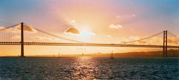 Suspension bridge over sea against sky during sunset