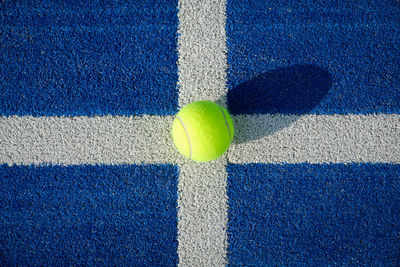 Yellow tennis ball in the court on blue grass - paddle tennis ball on the court on blue turf