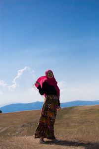 Side view of woman standing on rock against sky