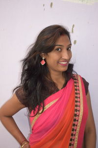 Portrait of smiling young woman in pink sari standing against wall