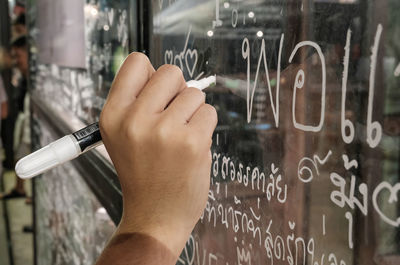 Cropped image of hand writing on glass window