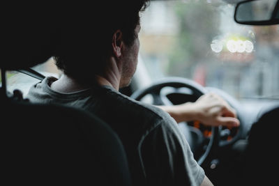 A young caucasian guy keeps his hand on the steering wheel while driving a car.