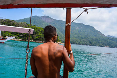 Shirtless man sitting on swing against lake