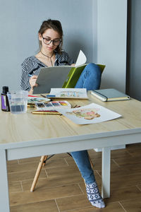 Millennial girl draws fabulous images on paper while sitting at home