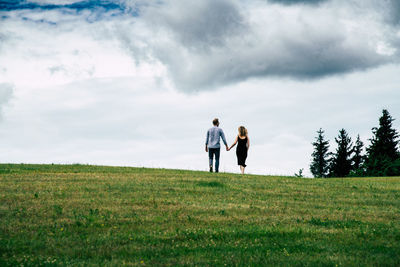 Rear view of couple standing on field against sky