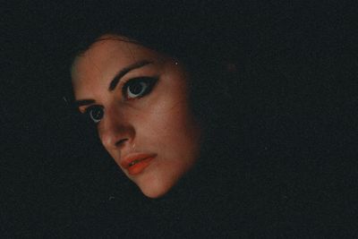 Close-up of young woman against black background