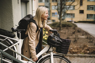 Side view of smiling businesswoman with backpack holding electric bicycle