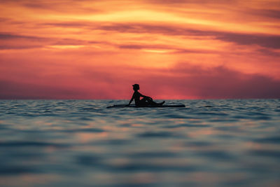Person in sea against sky during sunset