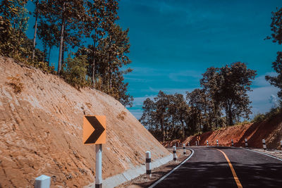 Road sign by trees against sky