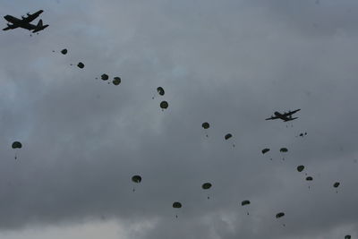 Low angle view of paratroopers parachuting from aircraft against cloudy sky