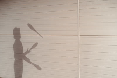 Side view shadow of anonymous talented male circus performer in hat juggling clubs near white wall