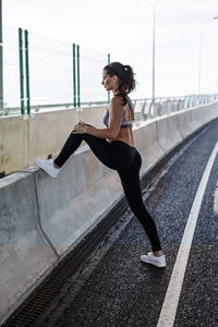 Full length of young woman exercising on bridge against sky