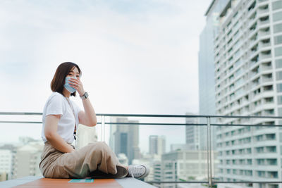 Solo asian woman wear protective mask during outdoor break and relax at rooftop with city background