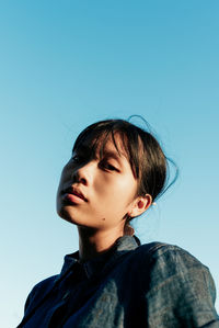 Portrait of woman looking away against blue sky