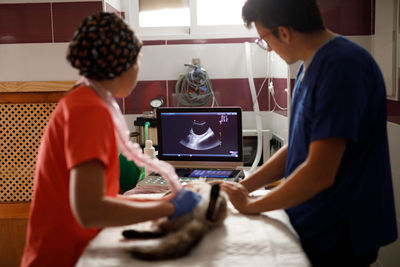 Side view of male and female vet doctors in uniforms examining cat with modern ultrasound in vet clinic