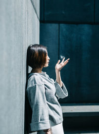 Side view of woman playing with flower while standing against wall