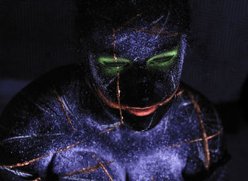 Close-up of woman with glowing face paint against black background