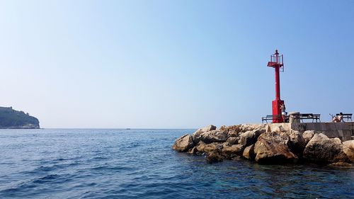 Lighthouse by sea against clear sky