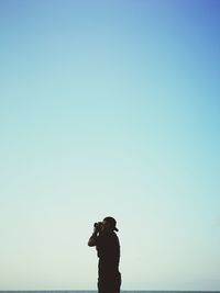 Man photographing sea against clear blue sky