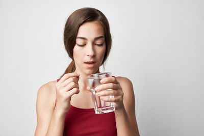 Young woman drinking glass against white background