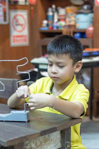 Boy holding metallic structure at desk in school