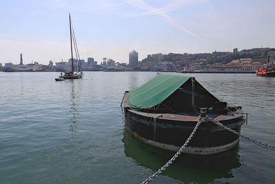 Sailboats moored in river against sky in city