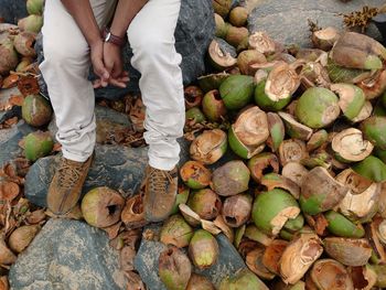 Low section of man sitting on rock by coconut shells