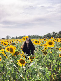 Woman standing amidst sunflower field against sky