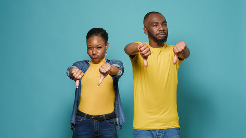 Man and woman showing thumbs down standing against wall