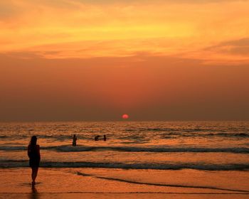 Silhouette man standing on beach against orange sky