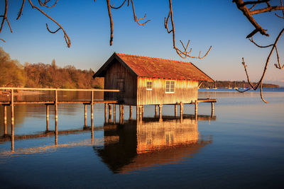 Wooden house on lake by building against sky