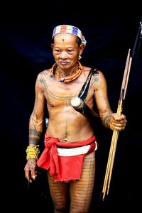 Shirtless mature man holding sticks against black background