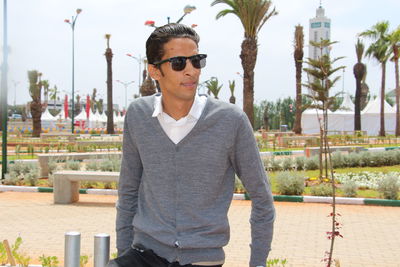 Young man wearing sunglasses standing against plants