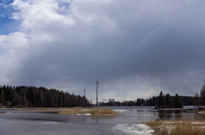 Windmills by lake against cloudy sky