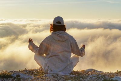 Rear view of woman sitting against sky during sunset