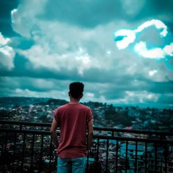 Rear view of man looking at cityscape against sky