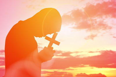 Side view of silhouette man holding cross against sky during sunset
