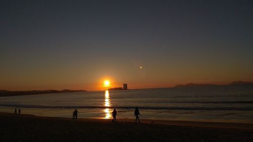 Silhouette people on beach against sky during sunset